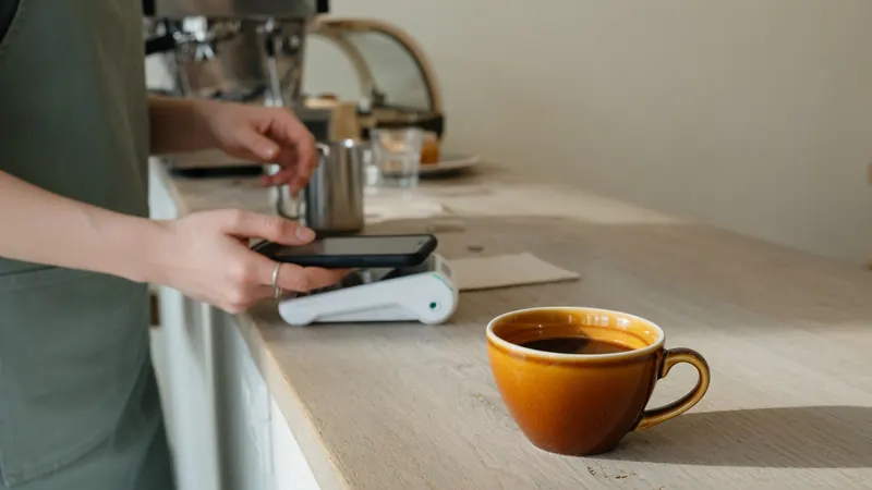 A customer paying with a phone at a cafe counter, an amber coffee cup in the foreground